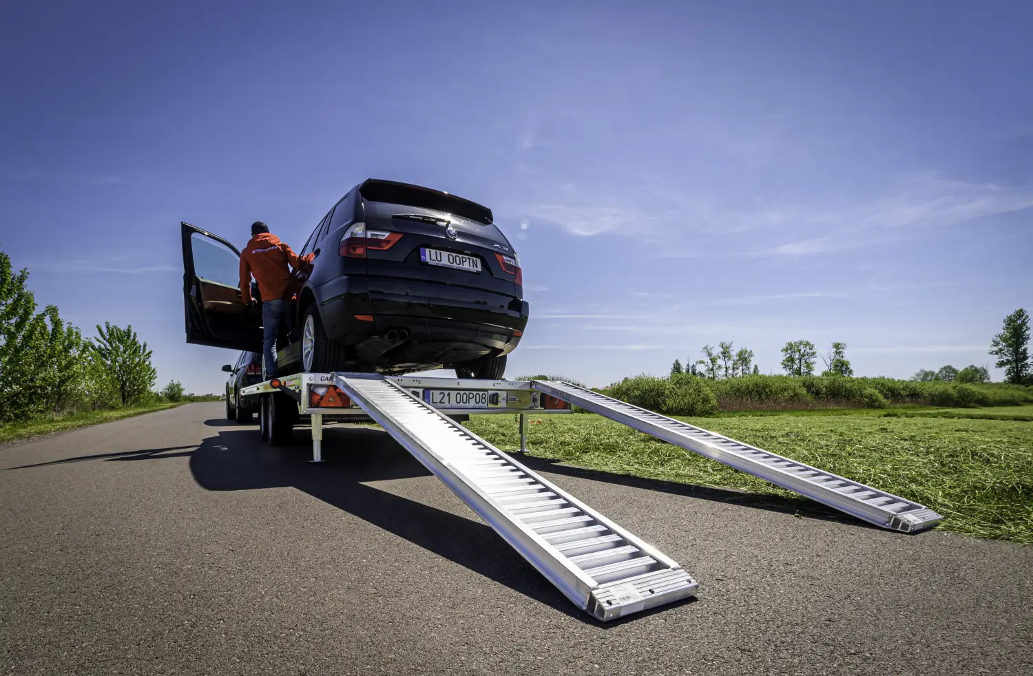 Czarny SUV załadowany na lawetę samochodową z rozłożonymi metalowymi najazdami na poboczu drogi.